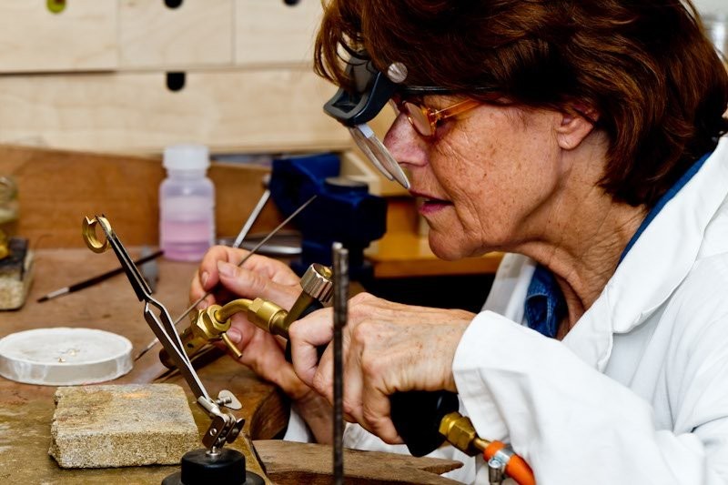 Olga Cordemeyer aan haar werkbank, met loep en brander, bezig met een sieraad
