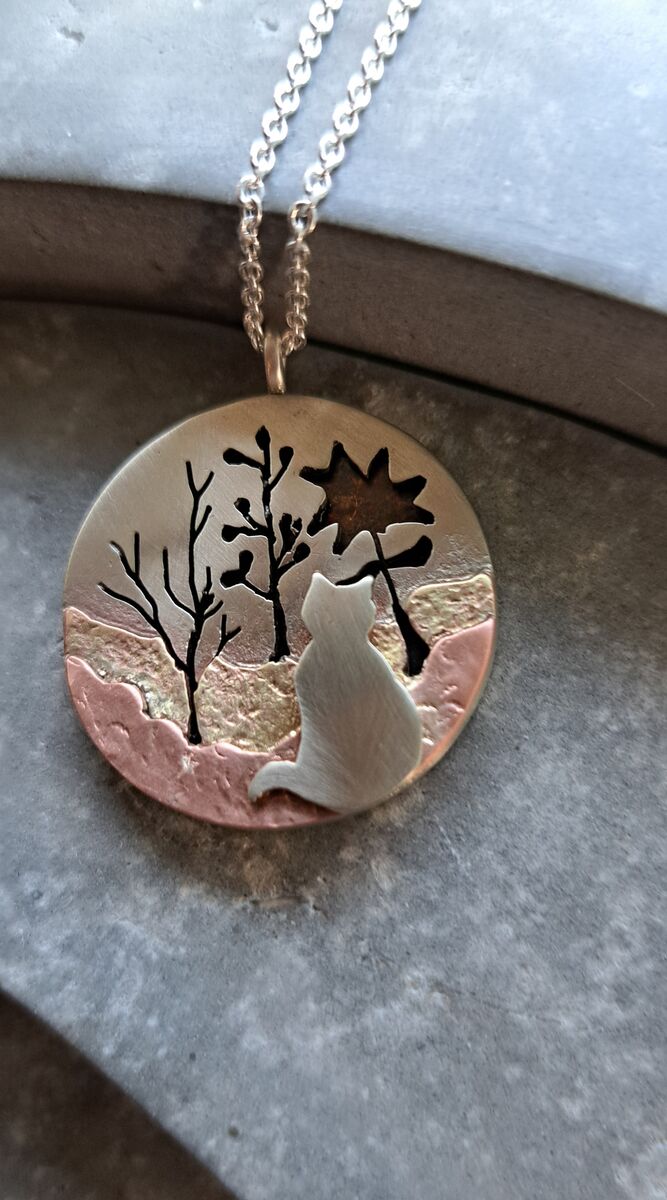 Ronde hanger met het silhouet van een kat, bomen en een zon, in zilver, koper en messing