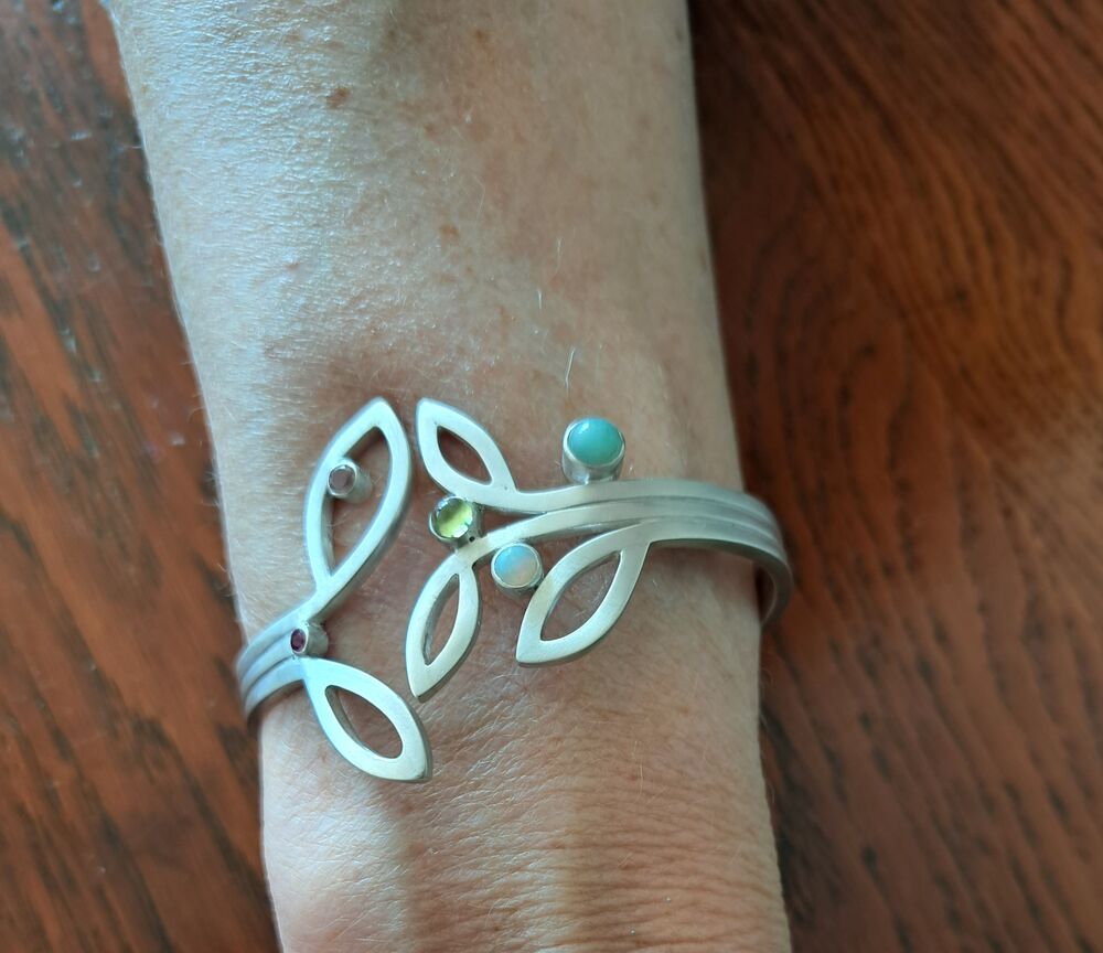 Zilveren manchet-armband met bladvormen en verschillende kleursteentjes, gedragen om de pols