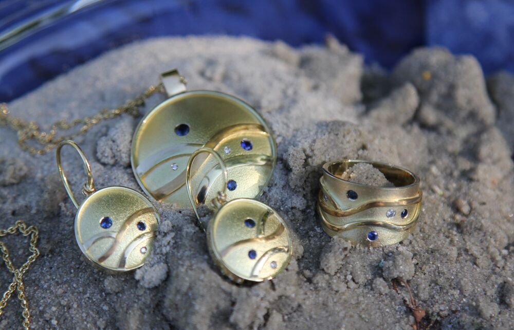 Set van gouden hanger, oorbellen en ring met saffieren en diamantjes, gefotografeerd op zand