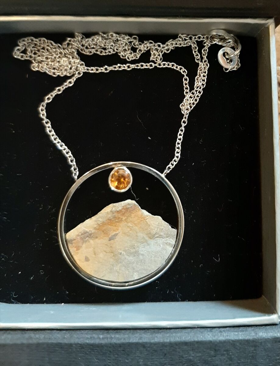 Zilveren cirkel met een ruwe steen en een oranje citrien als zon, aan een zilveren ketting